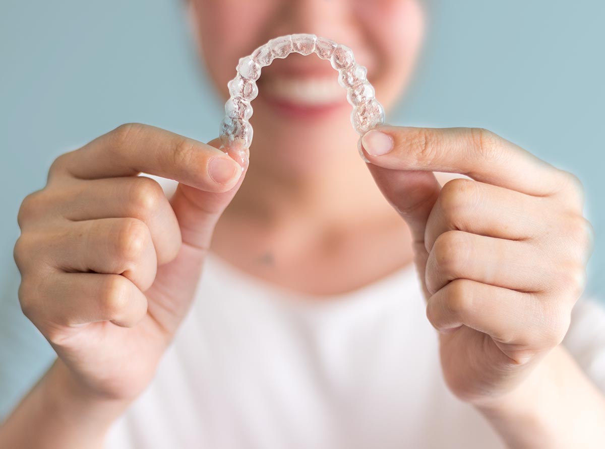 A smiling woman holding invisalign or invisible braces, orthodontic equipment