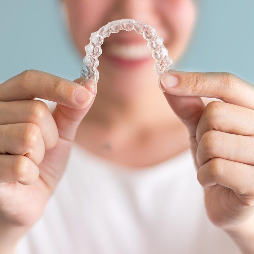 A smiling woman holding invisalign or invisible braces, orthodontic equipment