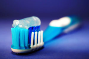 Close-up of a toothbrush with blue and white bristles holding a dollop of clear blue toothpaste; background features a soft blue gradient with the handle slightly blurred.